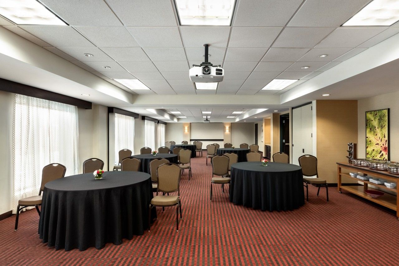 A conference room with multiple tables, chairs, a projector, and a large window with curtains.