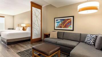 A hotel room with a bed, a sofa, an ottoman, a painting, and a ceiling light fixture.
