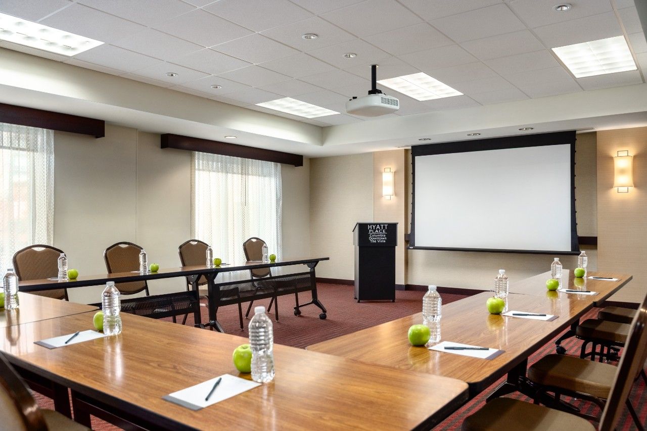 A conference room with a long table, chairs, a projector screen, and a podium.