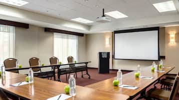 A conference room with a long table, chairs, a projector screen, and a podium.