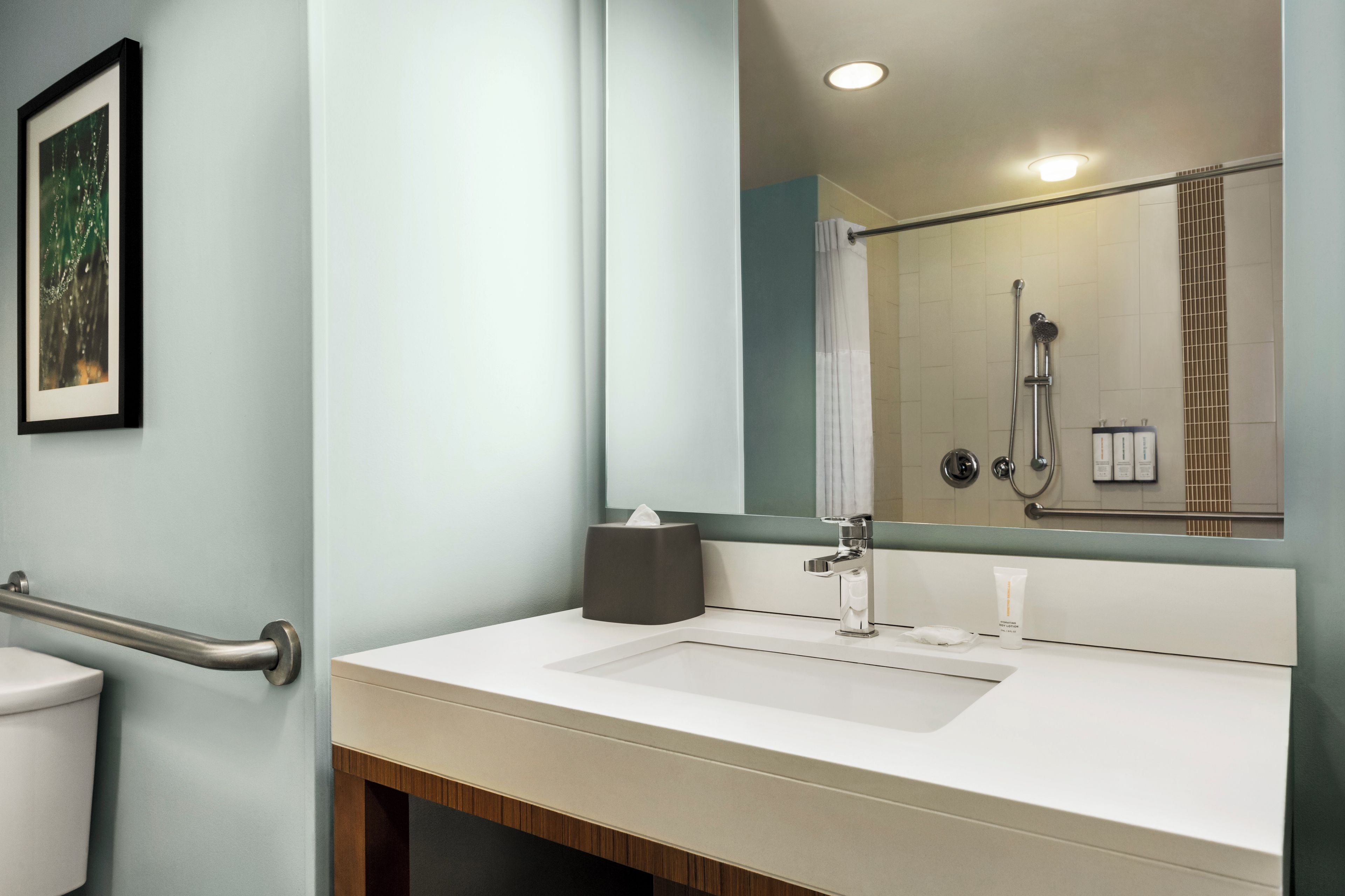 A modern bathroom with a white sink, a large mirror, and a shower visible in the reflection.