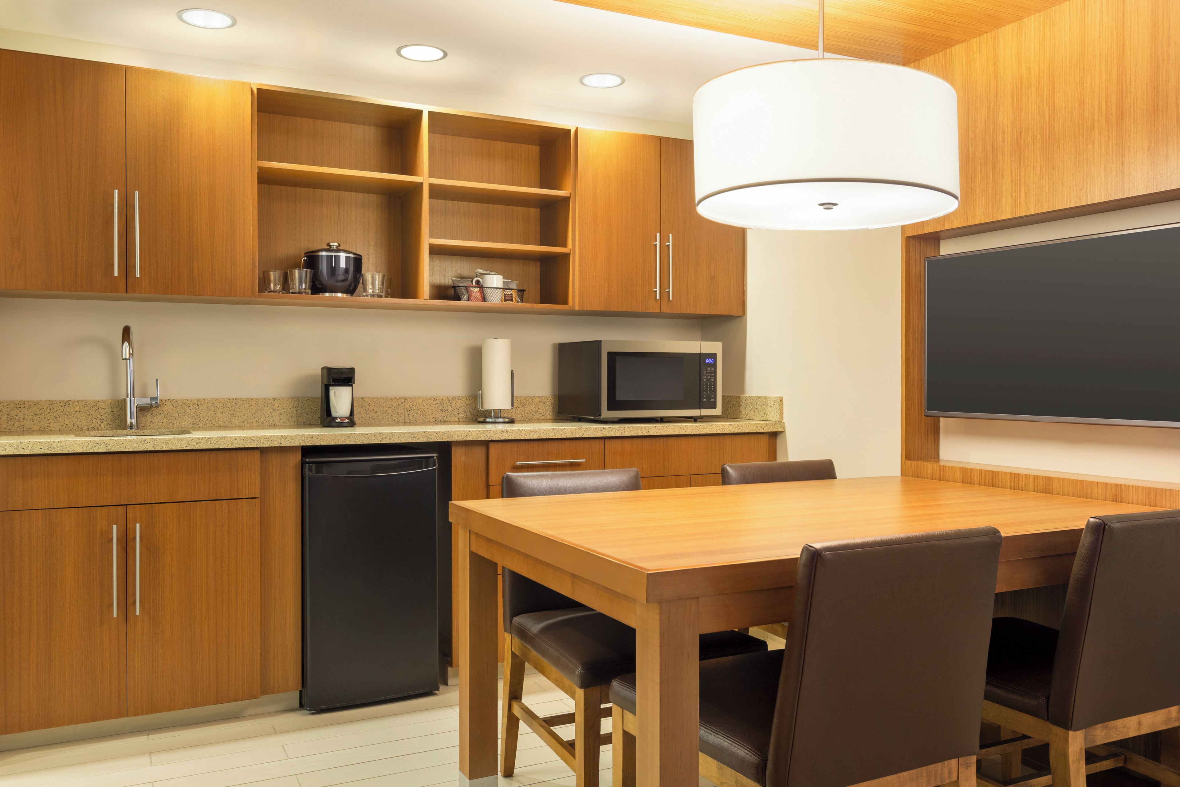 A modern kitchen with wooden cabinets, a black dishwasher, a microwave, and a dining table with chairs.