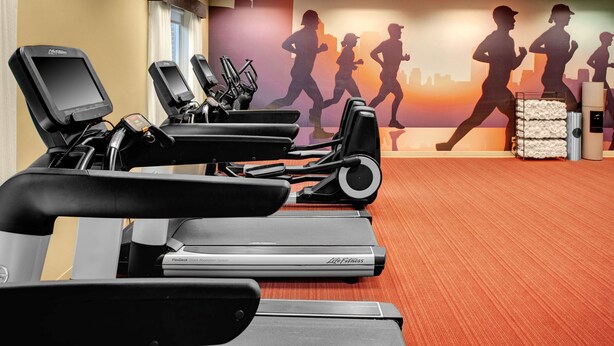Une salle de sport équipée de plusieurs tapis de course, ornée d’une fresque murale représentant des coureurs, et dotée d’un distributeur d’eau.