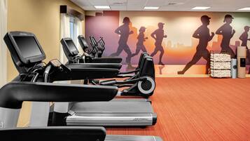 Une salle de sport équipée de plusieurs tapis de course, ornée d’une fresque murale représentant des coureurs, et dotée d’un distributeur d’eau.