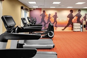 Une salle de sport équipée de plusieurs tapis de course, ornée d’une fresque murale représentant des coureurs, et dotée d’un distributeur d’eau.