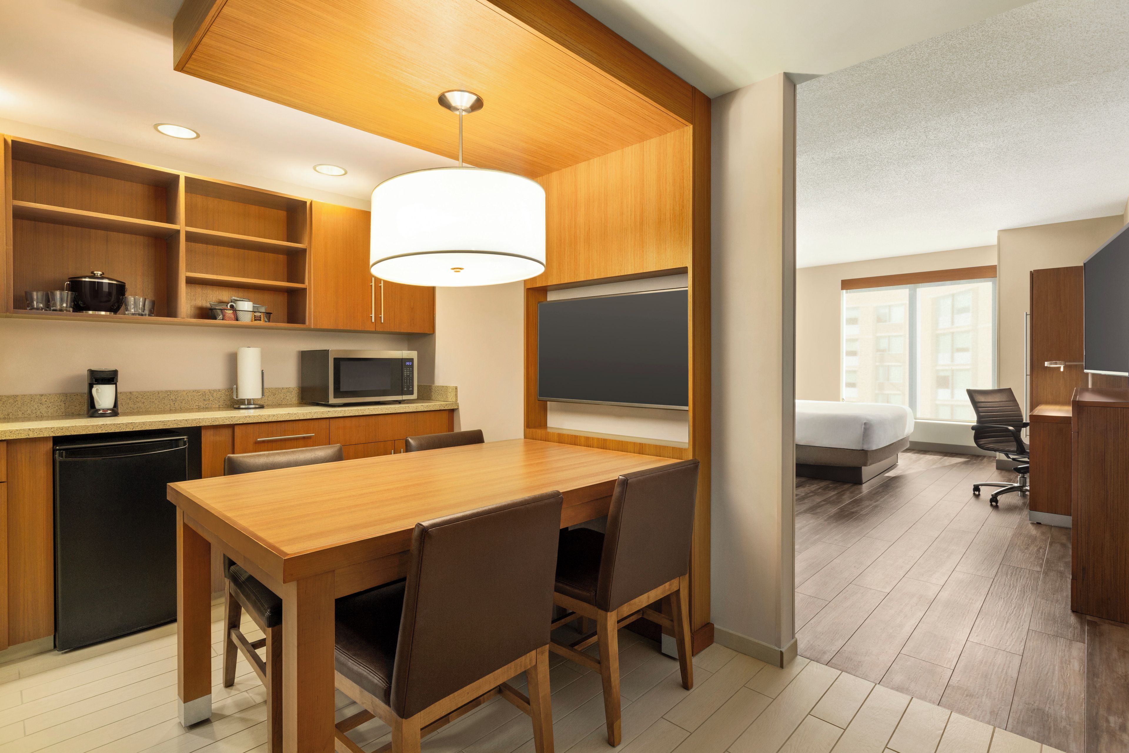A modern kitchen with wooden cabinets, a dining table with chairs, a microwave, and a coffee machine.