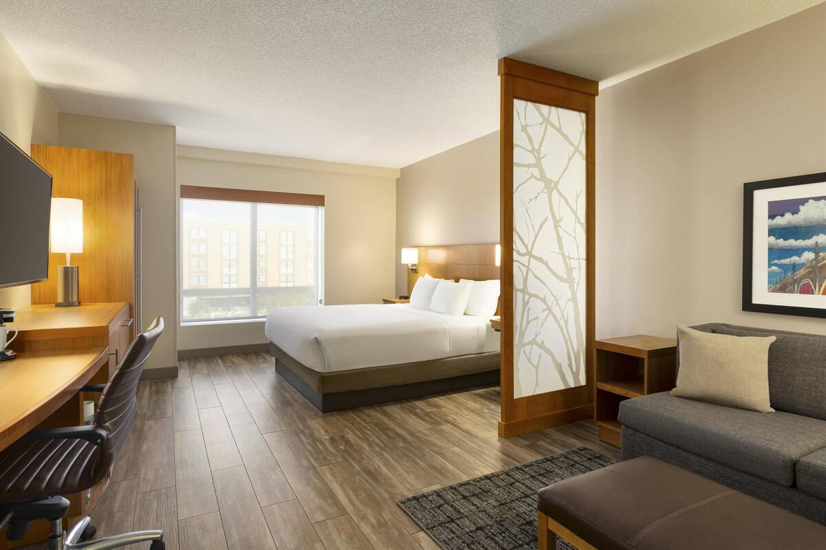 Een hotelkamer met een bed, bureau, stoel, bank en een groot raam.