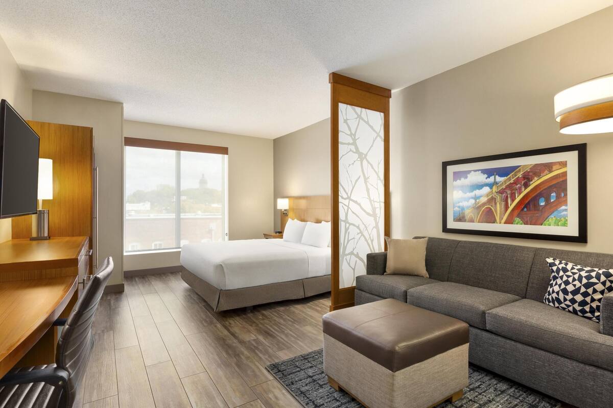 Een hotelkamer met een bed, een bank, een televisie, een bureau en een raam.