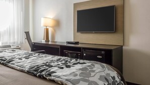 Habitación de hotel con cama, escritorio, silla, lámpara, televisor y aire acondicionado.