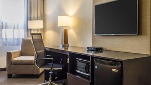 Habitación de hotel con escritorio, silla, televisor de pantalla plana, lámpara y microondas.