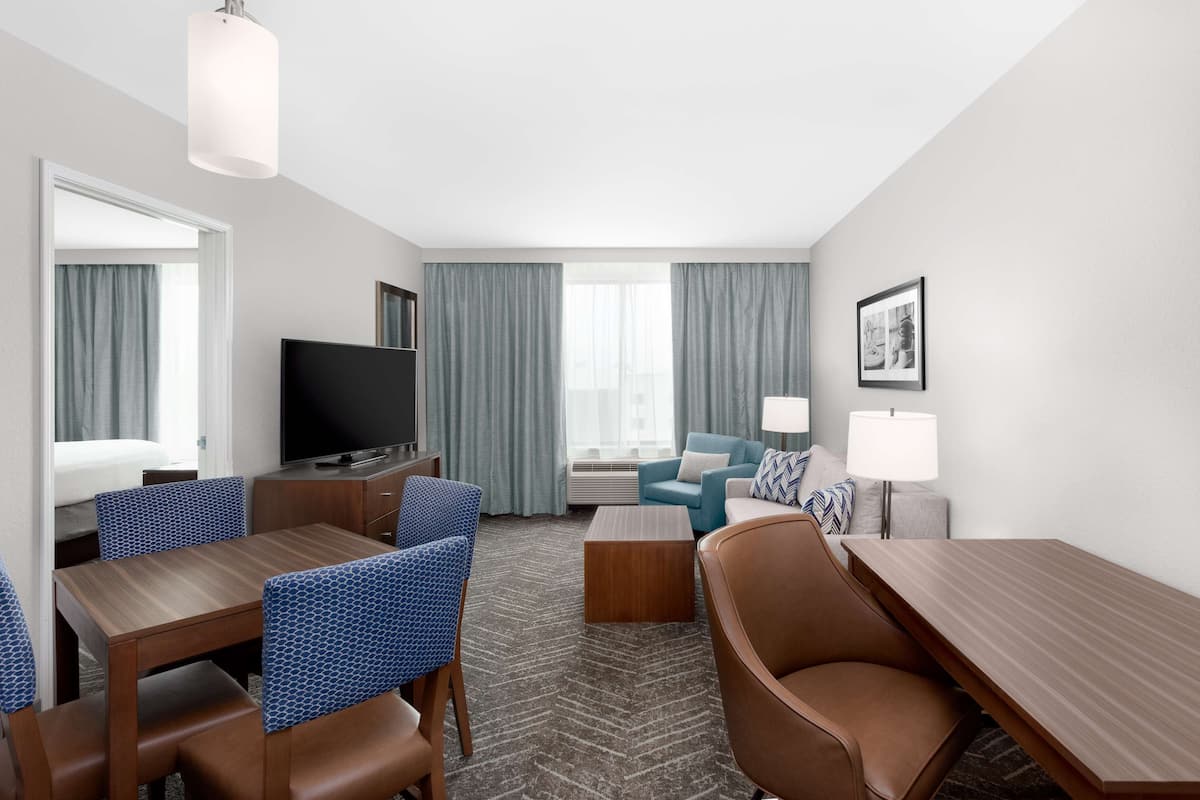 A hotel room with a dining area, a TV, a sofa, and a lamp.