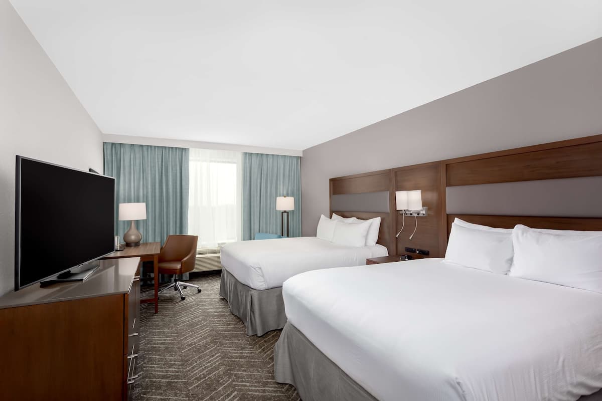 A hotel room with two beds, a desk with a TV, and a chair.