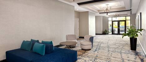 A spacious lobby with a blue sofa, two armchairs, a round table, and a potted plant.