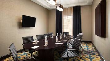 A conference room with a dark wooden table, black leather chairs, a flat-screen TV, and a patterned carpet.