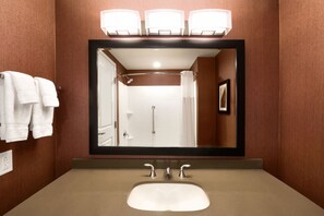 A bathroom with a large mirror, a sink, and a shower. There are towels hanging on the wall and a framed picture. - DoubleTree by Hilton Charleston Mount Pleasant (Mount Pleasant)