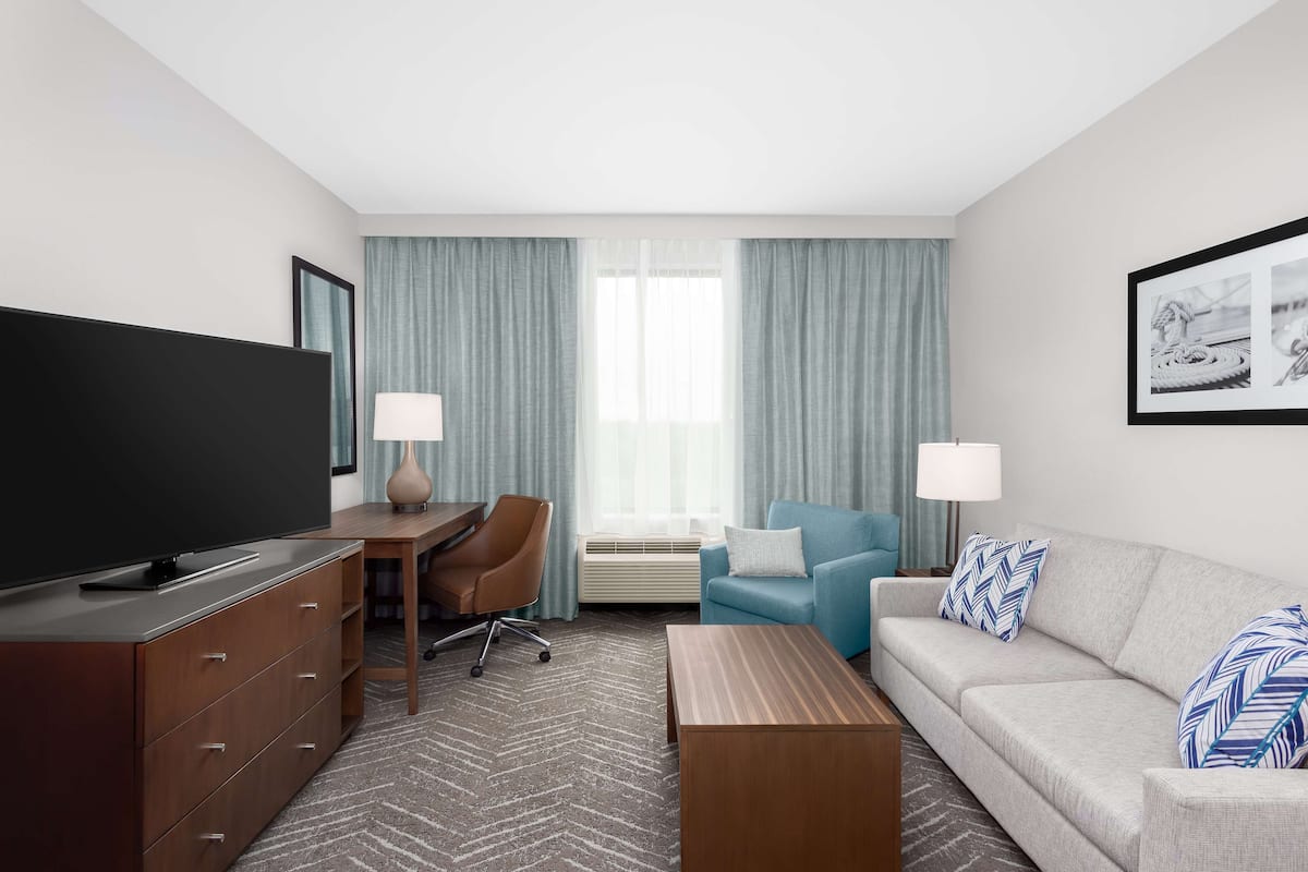 A modern hotel room with a flat-screen TV, a wooden desk, a blue sofa, and a large window with curtains.
