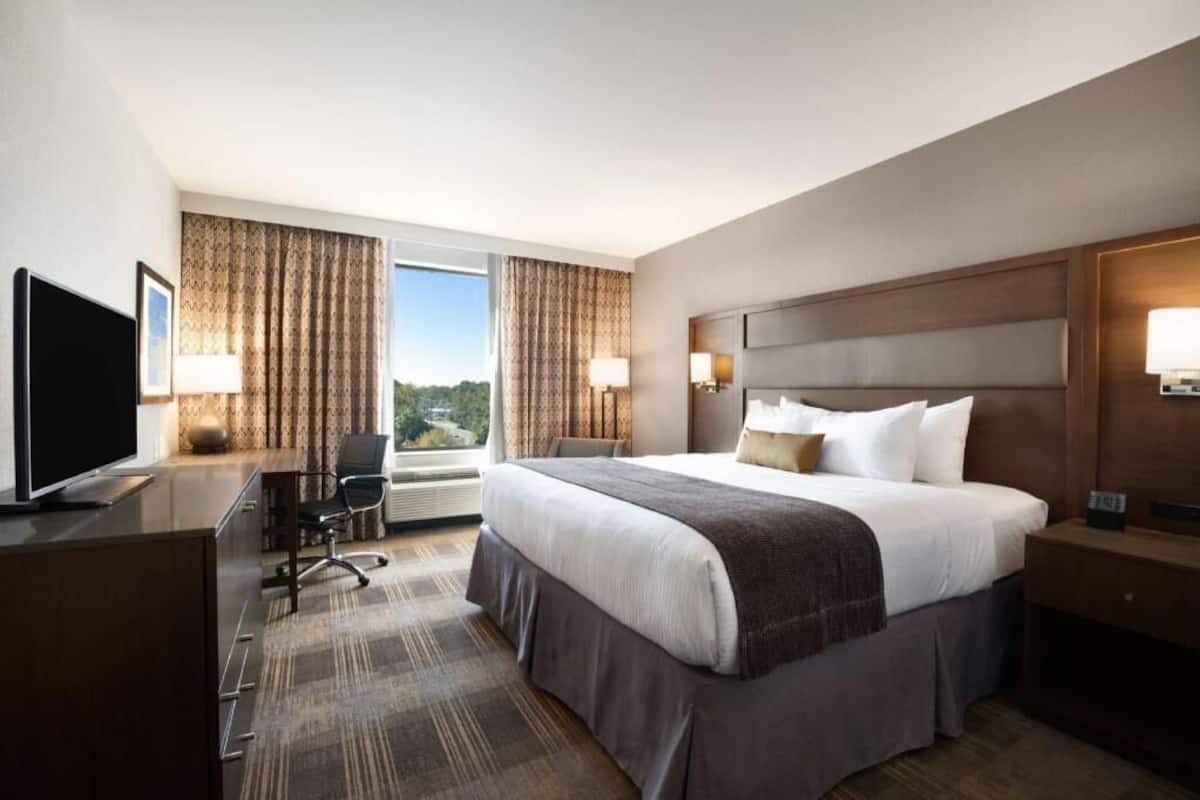 A hotel room with a bed, desk, chair, and a television.