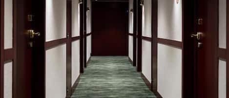 A hotel hallway with a green carpet, wooden doors, and recessed lighting.