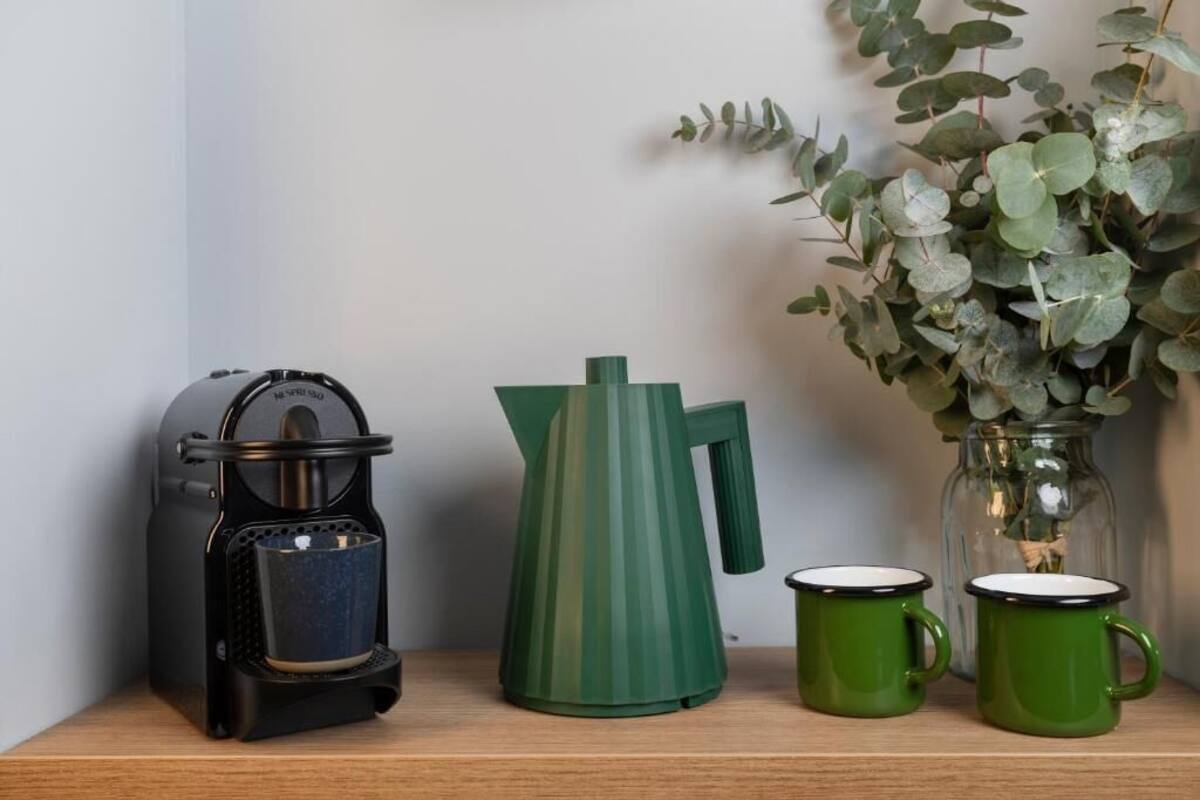 Une étagère avec une bouilloire noire, une bouilloire verte et deux tasses vertes.