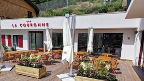 An outdoor seating area with wooden tables and chairs, surrounded by planters with flowers.