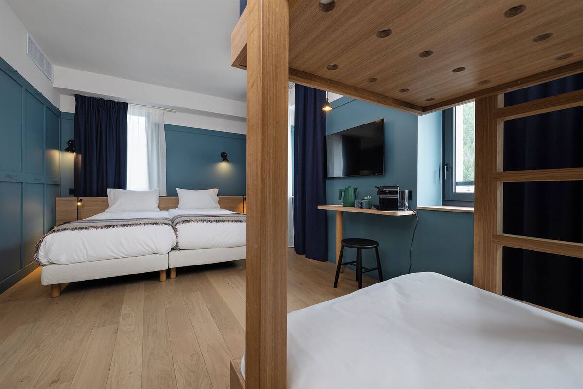 Une chambre d’hôtel moderne avec un plafond en bois, deux lits, un bureau avec une chaise, une télévision et de grandes fenêtres.