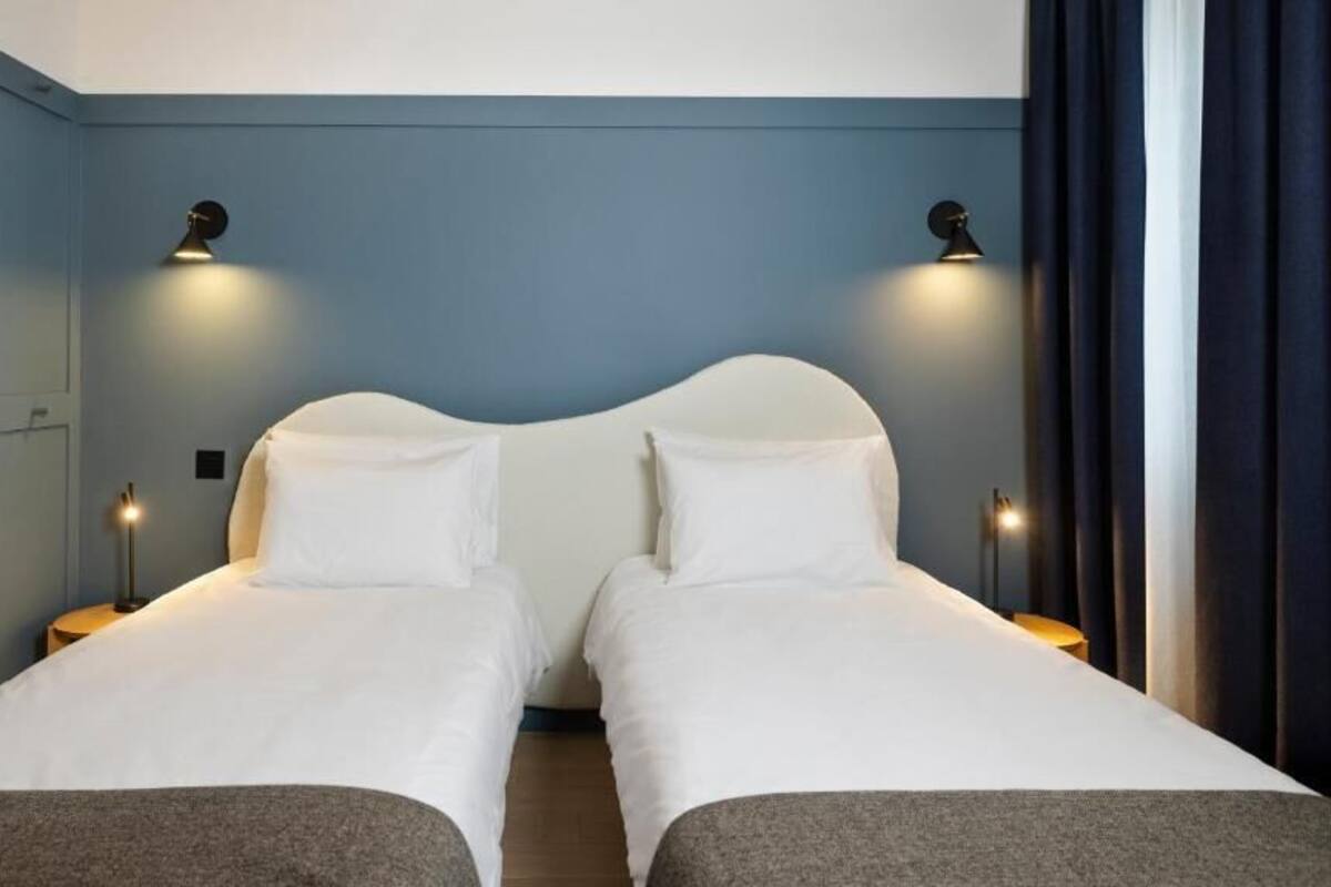 Une chambre double avec deux lits, chacun équipé de draps blancs et de lampes de chevet.