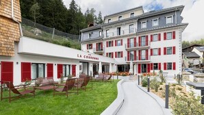A hotel with a white facade, red shutters, and outdoor seating.
