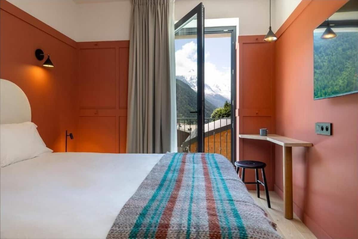 Une chambre avec un lit, un bureau et une vue sur les montagnes.