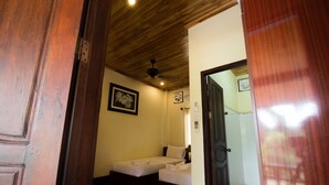 A room with two beds, wooden ceiling, and a door leading to another room. - Villa Somphong (Luang Prabang)