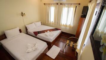 A hotel room with two beds, a wooden floor, an air conditioner, a television, and a window with curtains.