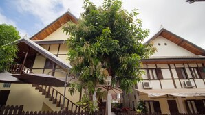 A traditional building with a wooden staircase, a fence, and a tree in front. - Villa Somphong (Luang Prabang)