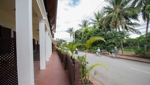 A street view with a sidewalk lined with potted plants and a building with a tiled walkway. - Villa Somphong (Luang Prabang)
