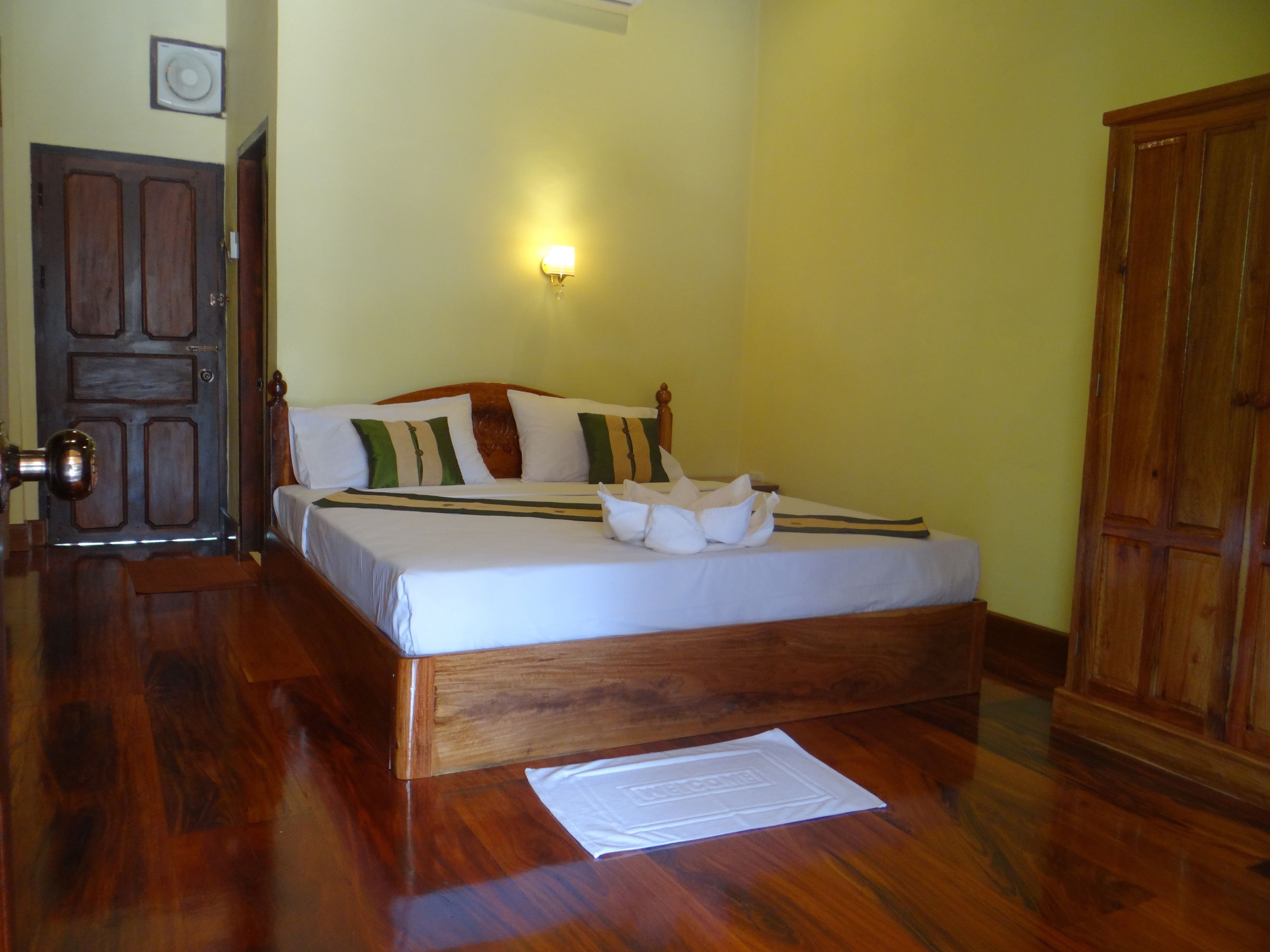 A neatly made bed with a wooden headboard, a wall-mounted light fixture, and a wooden wardrobe.
