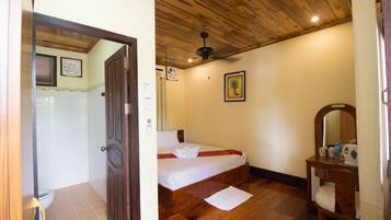 A bedroom with a wooden ceiling, a bed, a bedside table with a mirror, and a bathroom with a toilet and shower.