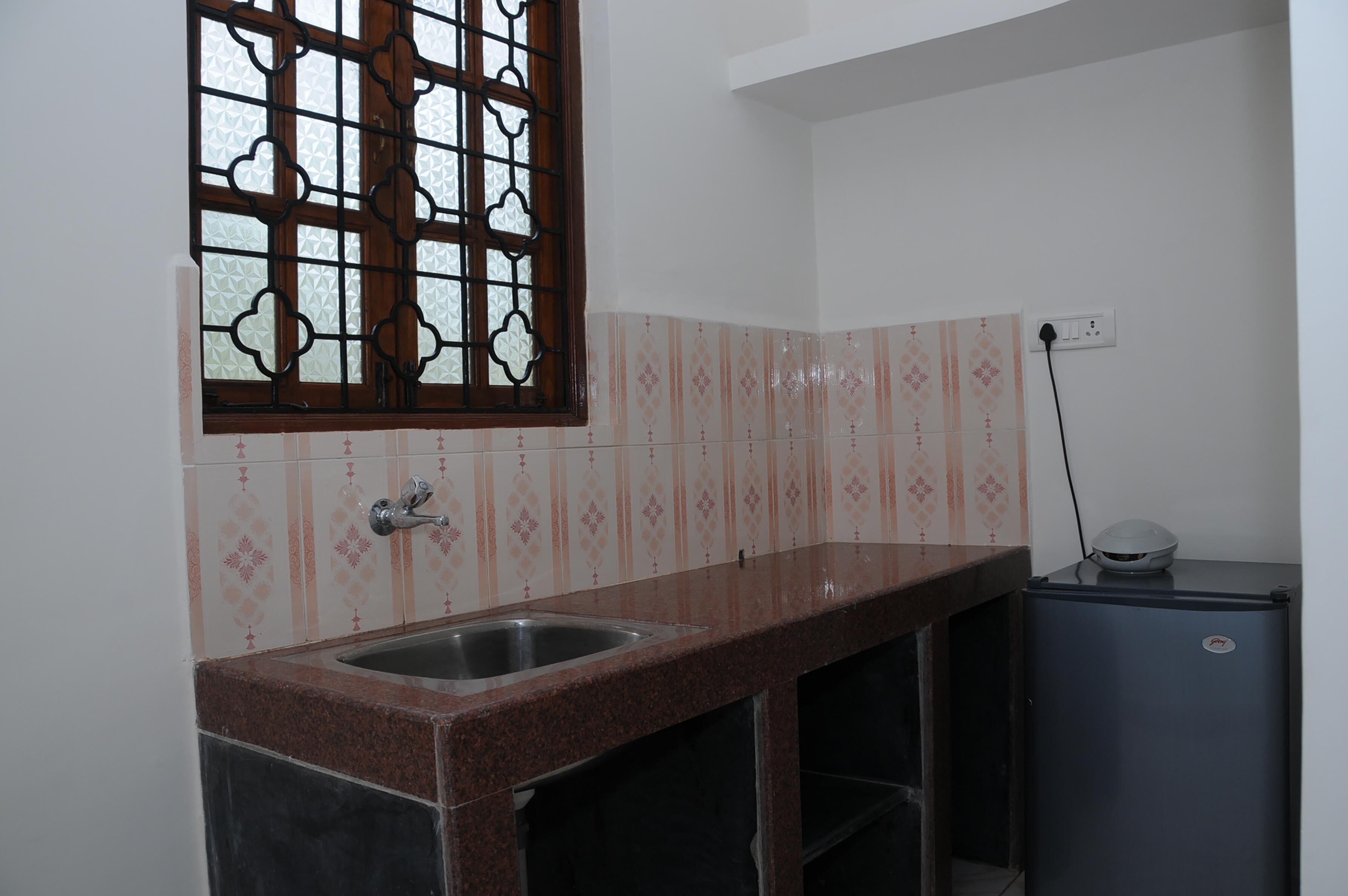A kitchen with a granite countertop, a sink, a window with a decorative grill, and a refrigerator.