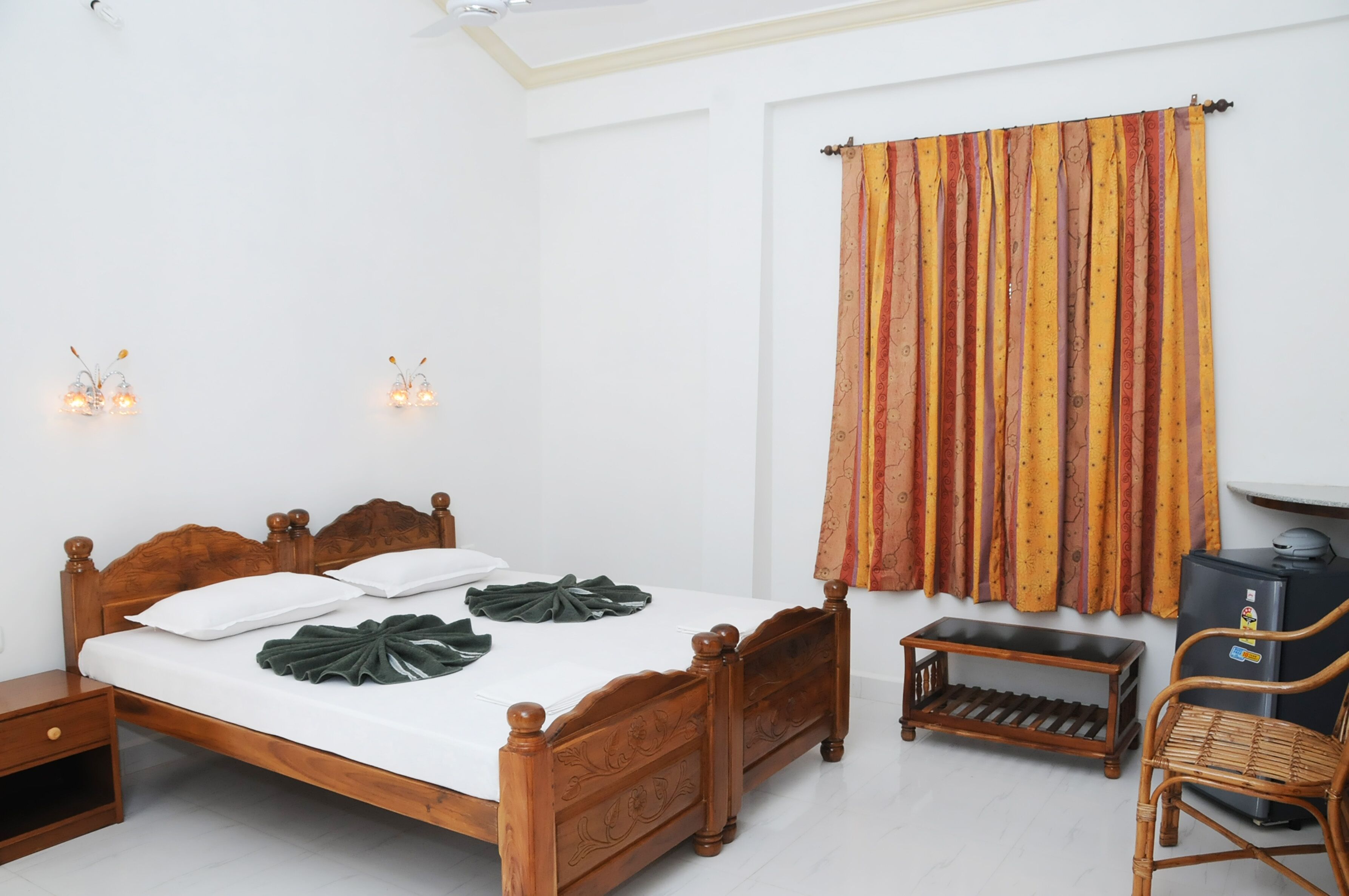 A neatly made bed with a wooden headboard, a small bedside table, a chair, and a wall-mounted TV.