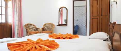 A hotel room with two beds, each with an orange towel, a wooden wardrobe, a mirror, and a window with curtains.