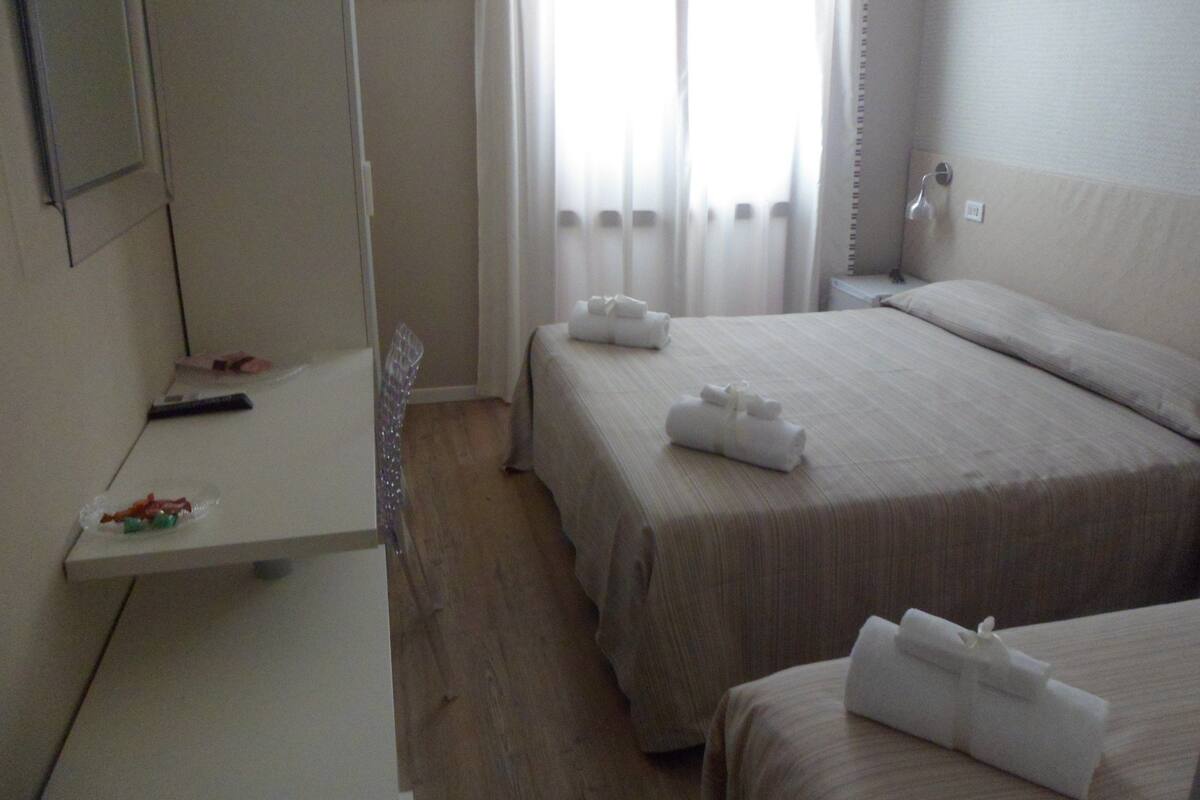 A hotel room with two beds, a small desk, and a mirror.