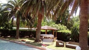 Ein Poolbereich mit Gazebo, Gartenmöbeln und Palmen.