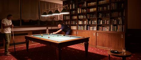 A pool table in a room with a large bookshelf and a mirror.