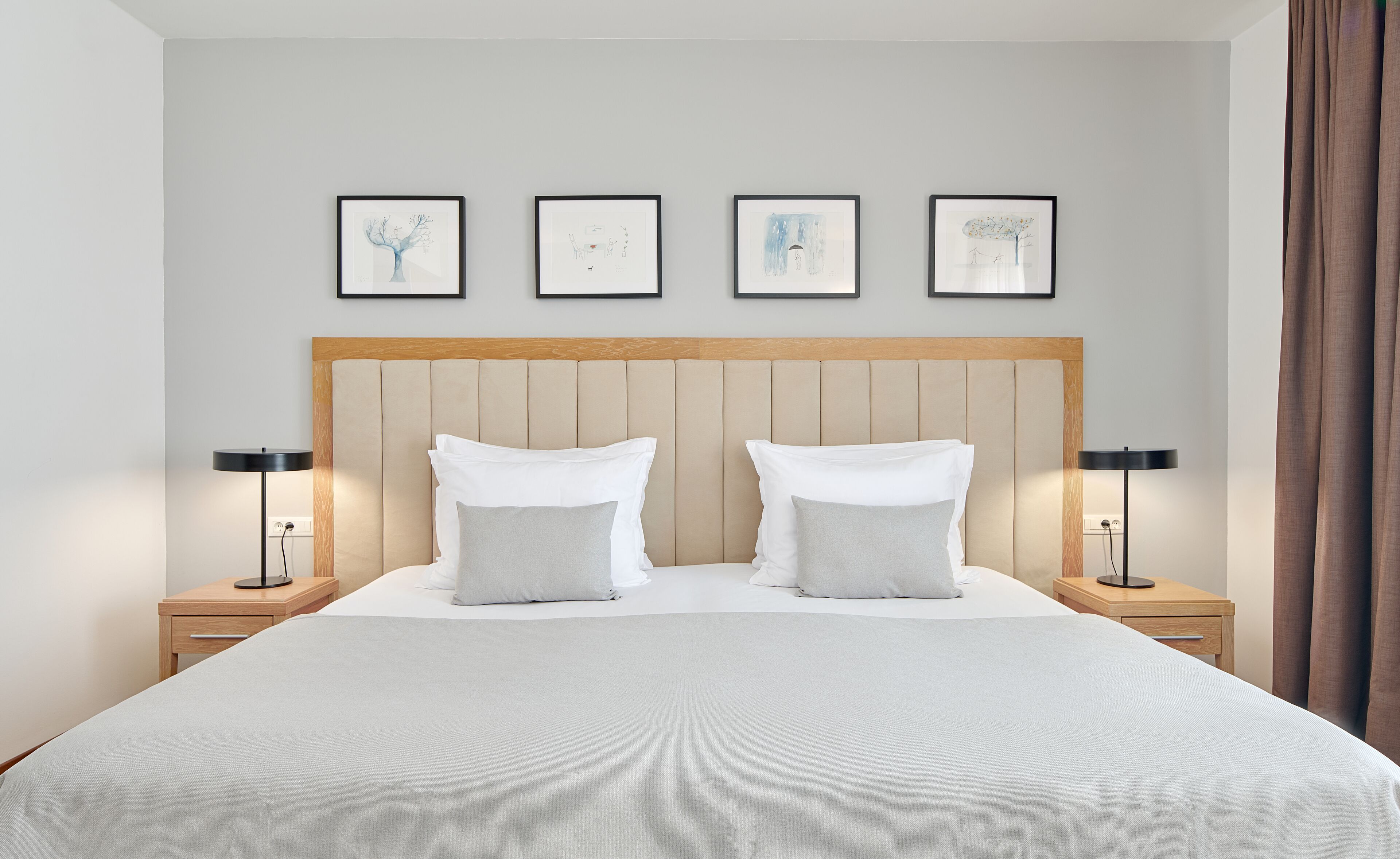Habitación de hotel con una cama grande, dos mesitas de noche y cuatro obras de arte enmarcadas en la pared.