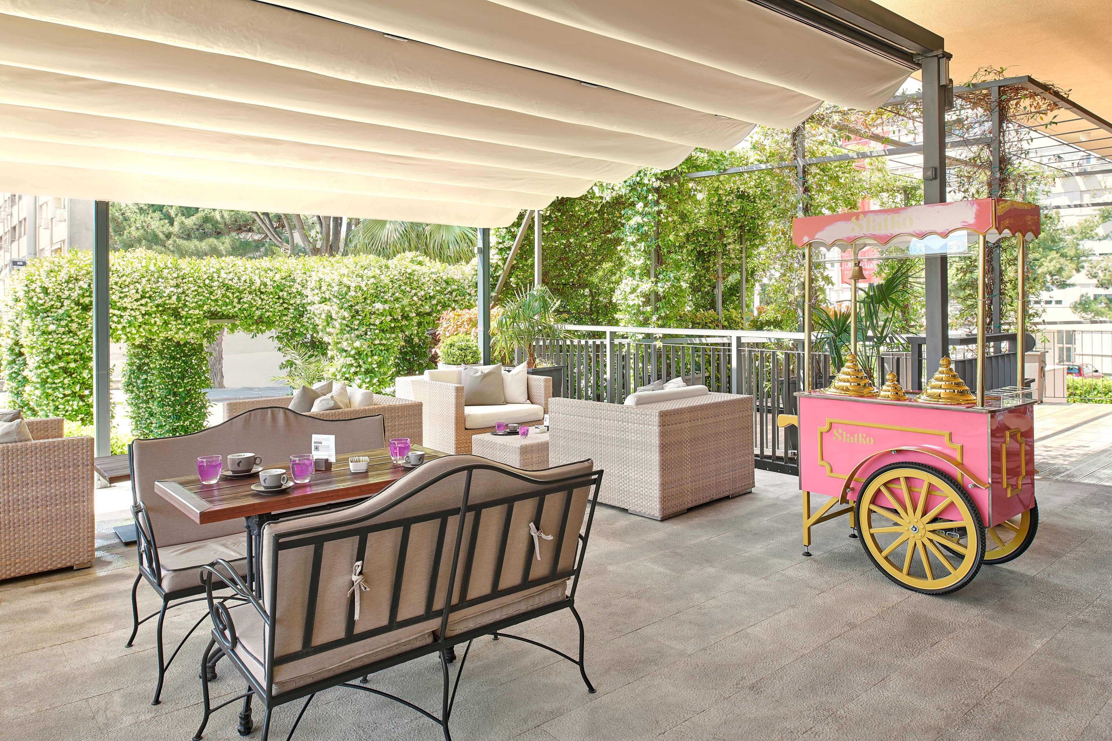 An outdoor seating area with wicker furniture and a pink cart.