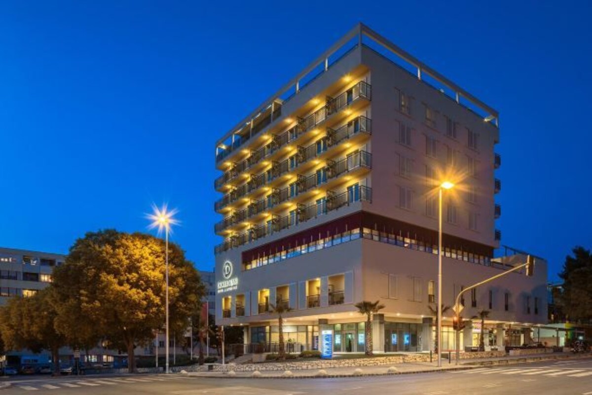 Un hôtel à plusieurs étages, doté de balcons, avec une entrée au niveau du sol et un ciel dégagé.