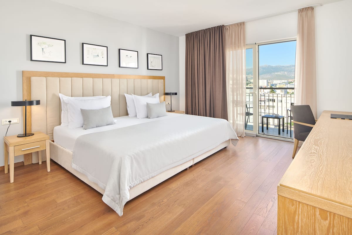Habitación de hotel con una cama grande, una mesita de noche, un escritorio y un balcón con vistas.