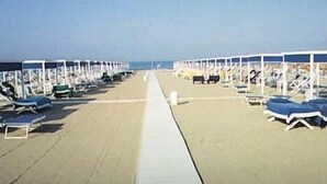 Ein Strand mit Reihen von Liegestühlen und Sonnenschirmen, einem klaren Himmel und einem sandigen Weg zum Wasser.