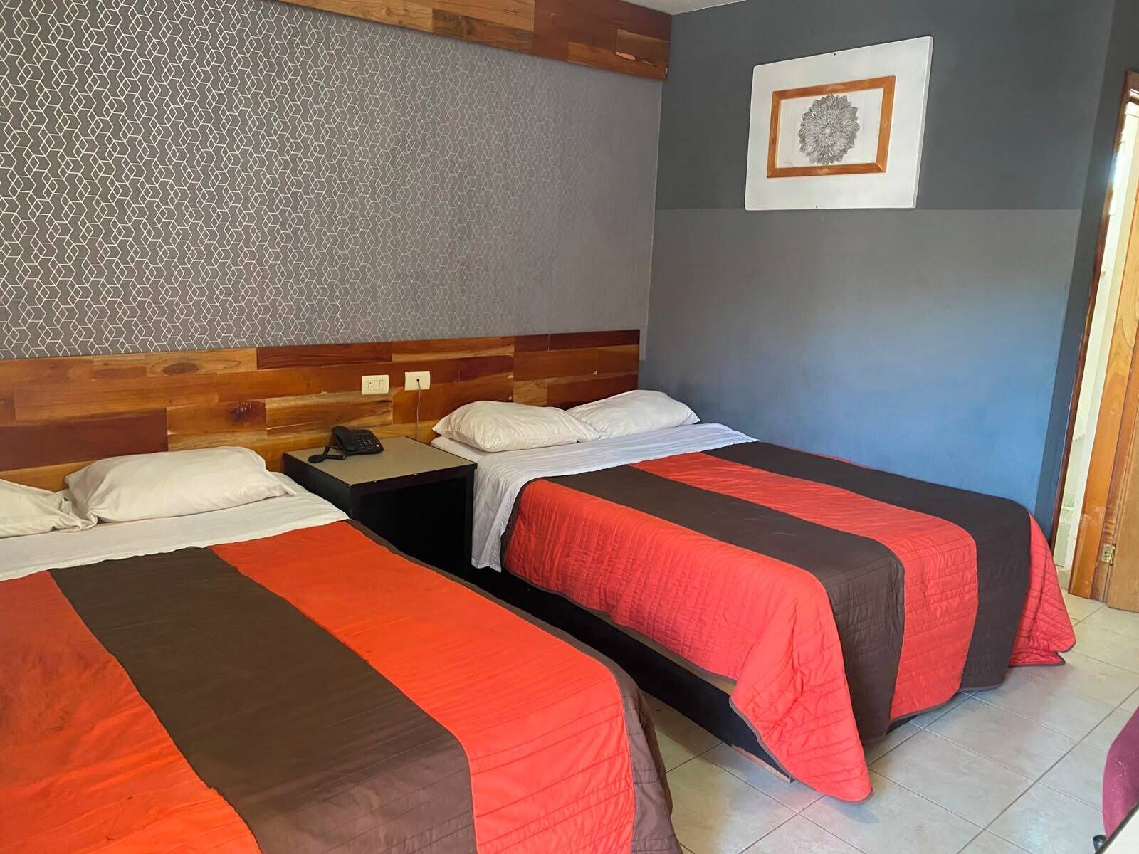 A hotel room with two beds, a wooden headboard, a patterned wall, and a framed artwork.