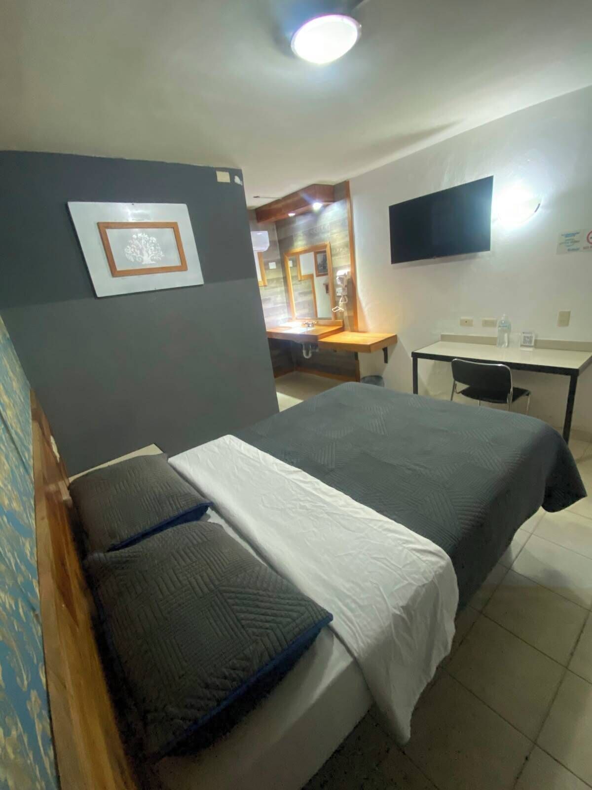 Habitación de hotel con cama, escritorio, silla, televisor y baño a la vista.