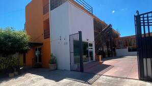 Un edificio con techo plano, entrada con portón y patio de concreto.