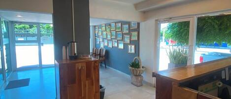 Un hall espacioso con una mesa de recepción, una pared decorada con cuadros enmarcados y un gran ventanal con vistas al exterior.