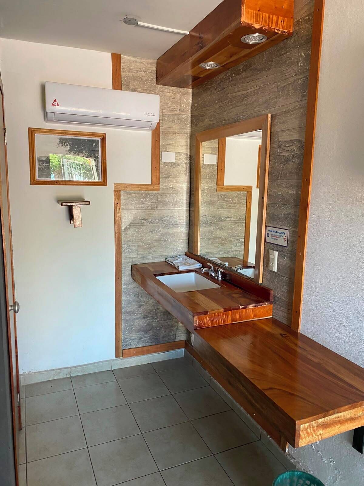 Uma casa de banho com toucador de madeira, um espelho grande e ar condicionado fixado à parede.